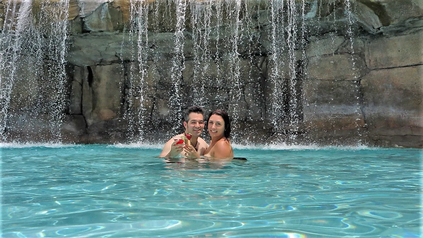 A couple under the waterfall in the Caliente pool